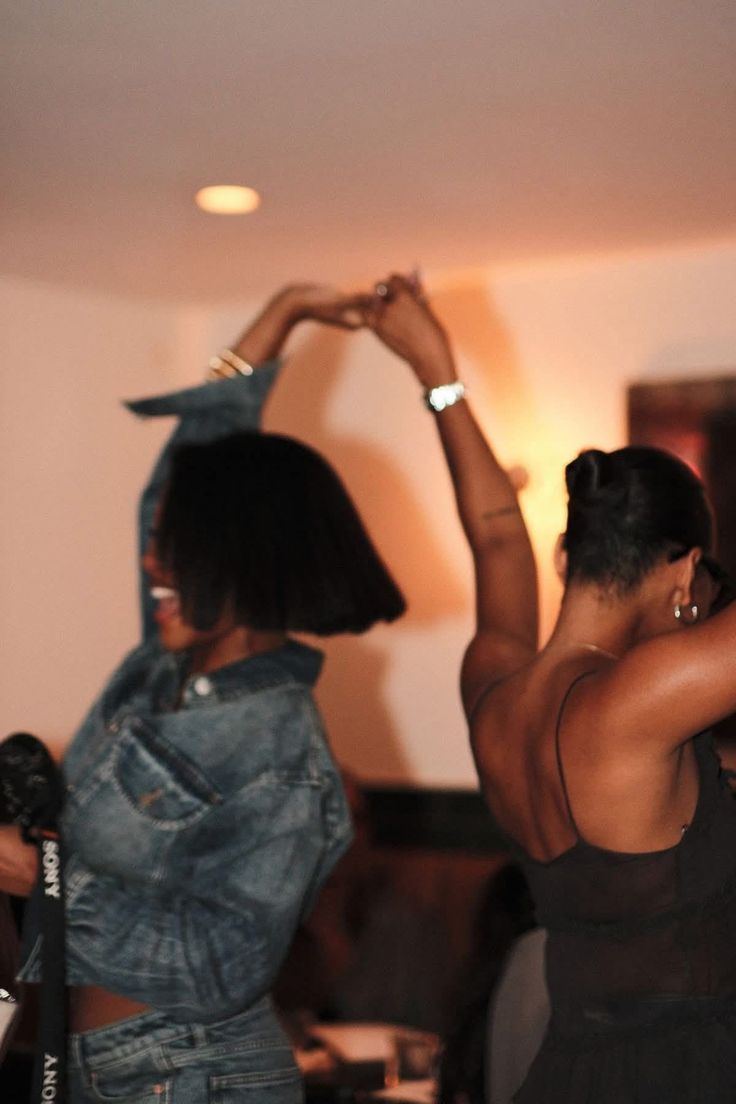Two women dancing with their hands joined overhead at an evening gathering