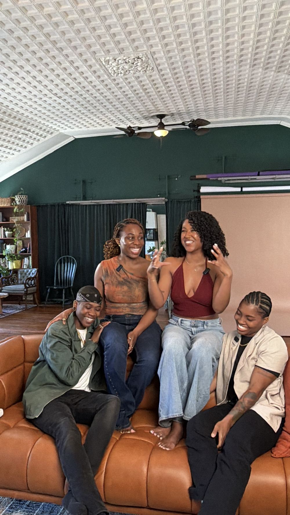 From left: Rae, Davina, Briana, and Dahnaya laughing together on a leather sofa in a studio